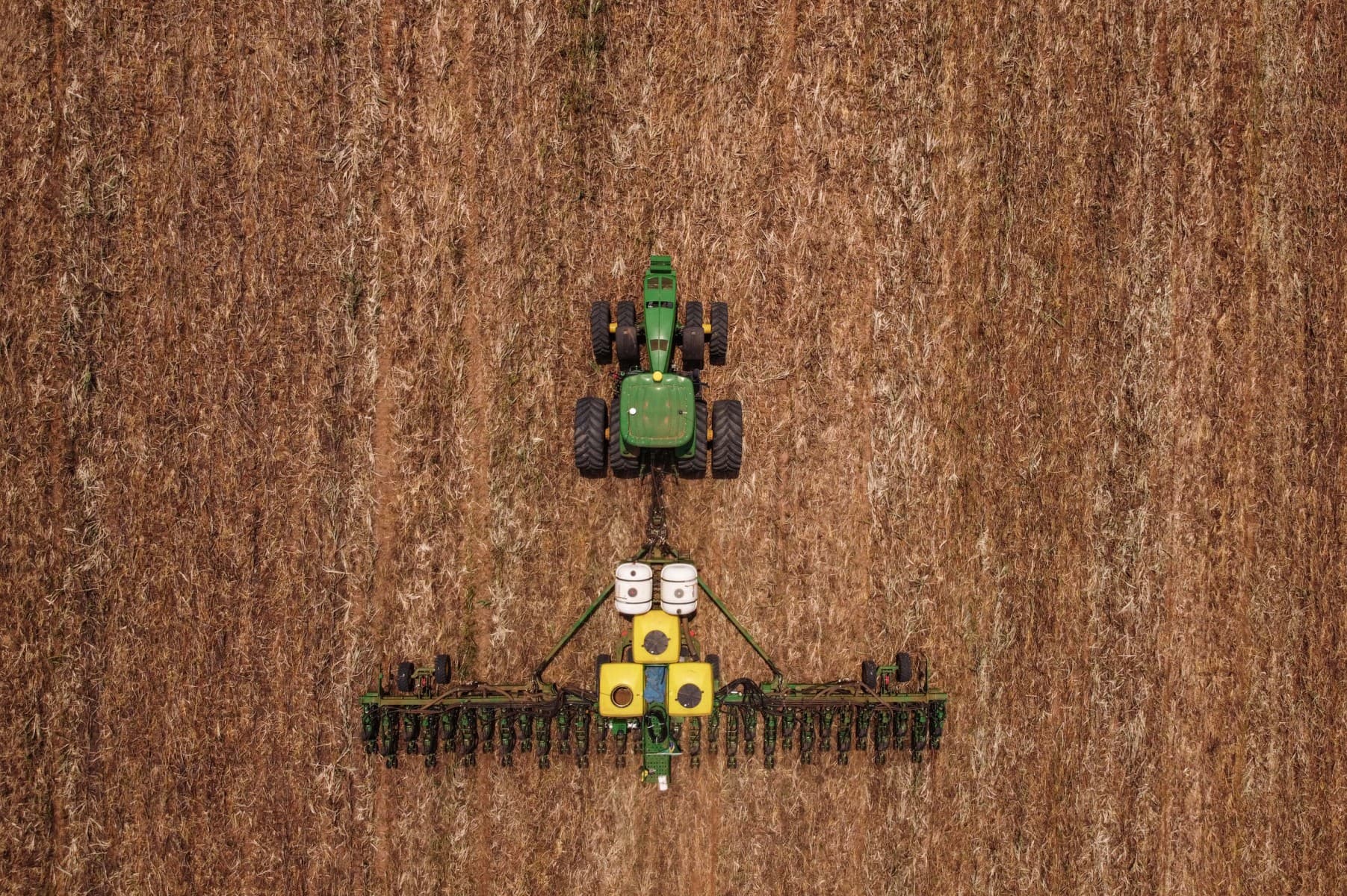 Vista aérea de um trator com plantadeira trabalhando em uma lavoura